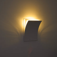 Modern wall-mounted light fixture casting a warm glow on a plain wall.