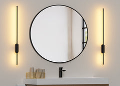 Round mirror with two wall lamps on a neutral wall in a bathroom setting.